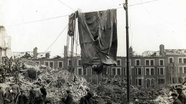 Residents and A.R.P. Wardens assist with the clearup in the rubble at the junction of Hillman Street and Antrim Road while the parachute of a mine hangs from overhead cables.