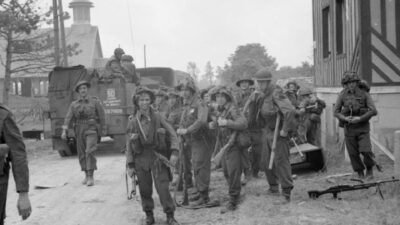 Soldiers of 3rd Infantry Division including Dubliner Charles Feeney (with Bren Gun) of 2nd Battalion, Royal Ulster Rifles pause at La Bréche d'Hermanville as they move inland during the Normandy landings. The half-track is from No. 246 Field Company, Royal Engineers.