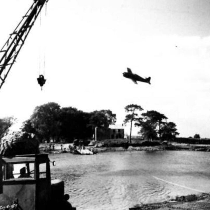 A plane simulates a dive bombing attack on a loaded ferry crossing the river during Exercise Judy at the River Bann, Newferry, Co. Antrim.