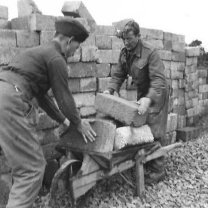 Members of The Pioneer Corps load a barrow of blocks used for the construction of Nissen huts at an airfield in Northern Ireland.