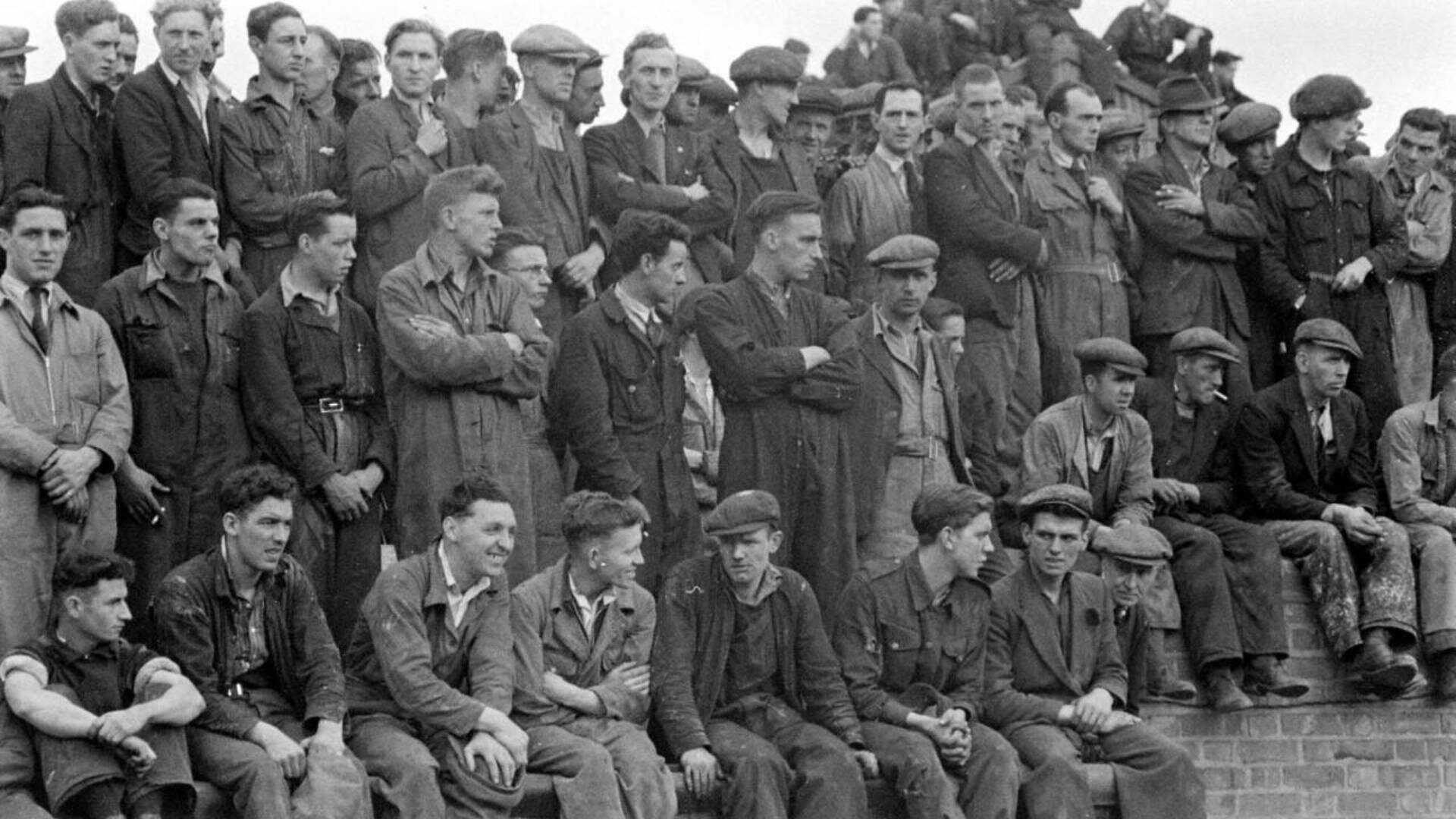 Civilians in workwear, most likely employees of the Harland and Wolff Ltd. shipyard in Belfast have an excellent vantage point to watch the arrival of H.M.S. Phoebe at Musgrave Channel, Belfast.