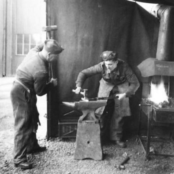 Craftsman Bellew of Tottenham, London, England and Craftsman E.W. Cook of Woodford, Essex, England at work in a blacksmith's shop at 3 Non Divisional Engineers, Royal Electrical and Mechanical Engineers base workshop at Gilford, Co. Down.