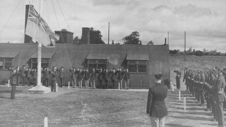 Personnel of the Royal Air Force and United States Army Air Force salute the lowering of the ensign as R.A.F. Toome becomed U.S.A.A.F. Station 236 at Toome Airfield, Co. Antrim on 26th July 1943.