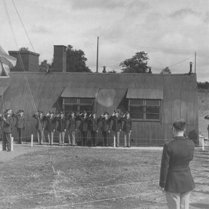 Personnel of the Royal Air Force and United States Army Air Force salute the lowering of the ensign as R.A.F. Toome becomed U.S.A.A.F. Station 236 at Toome Airfield, Co. Antrim on 26th July 1943.