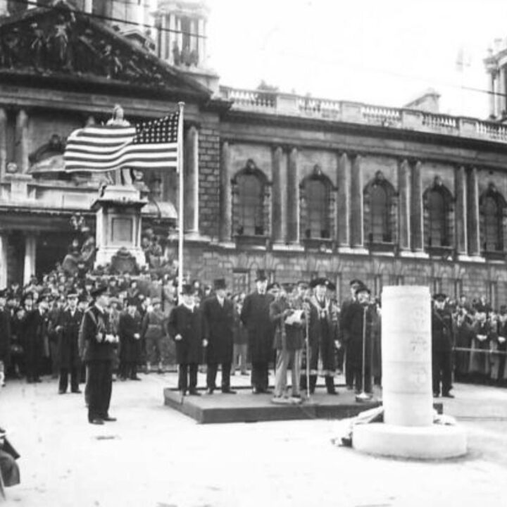 Major-General Russell P. Hartle (U.S. Army) adresses the crowd from a platform party including Sir James Grigg K.C.B., K.C.S.I, P.C. (Secretary of State for War) and the Duke of Abercorn (Governor of Northern Ireland) in the grounds of City Hall, Belfast. The occasion is the unveiling of a commemorative stone marking the first anniversary of the official arrival of U.S. troops to Northern Ireland and into the European Theater of Operation.