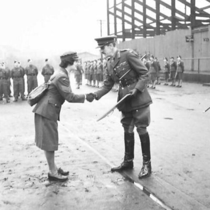 Brigadier P.H. Hansen V.C. presents a certificate for devotion to duty during an air raid to Sergeant Pauline Ann Bromwich of the Auxiliary Territorial Service. The event is the presentation of the St. Patrick's Day Shamrock by Brigadier P.H. Hansen V.C. to members of 31st Battalion Royal Ulster Rifles, U.S. Army Officers of Irish descent, and members of the Auxiliary Territorial Service at Dunmore Park, Belfast.
