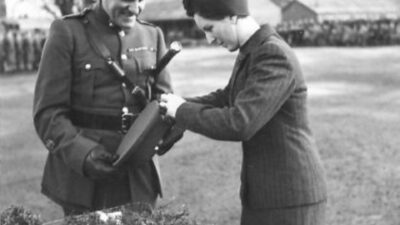 Mrs. Heard and Regimental Sergeant Major E.C. Jerome M.M. on his final parade as R.S.M. after 3.5 years service. The event is the presentation of the St. Patrick's Day Shamrock by Mrs. Heard, wife of Lieutenant Colonel R.A. Heard M.C., Commandant of 25th Infantry Training Centre to soldiers in Omagh, Co. Tyrone.