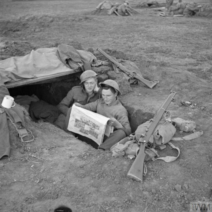 Fusilier Clarke of Marquis Street, Newtownards, Co. Down and Fusilier Hickey of Crumlin, Dublin, Ireland sit in a trench reading the Belfast published 'Ireland's Saturday Night'. 2nd Battalion, Royal Inniskilling Fusiliers celebrate St. Patrick's Day during their time in the fighting line at Anzio, Italy.