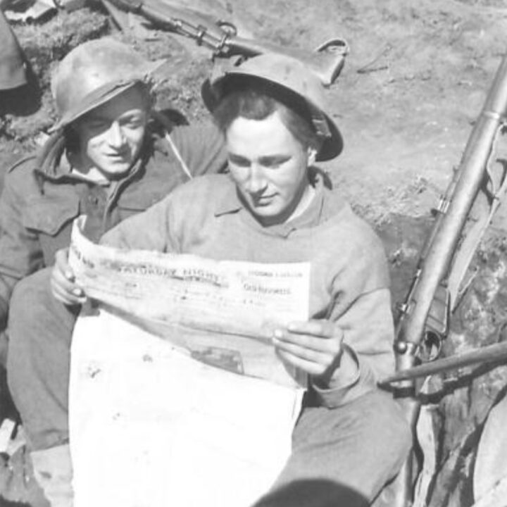 Fusilier Clarke of Marquis Street, Newtownards, Co. Down and Fusilier Hickey of Crumlin, Dublin, Ireland sit in a trench reading the Belfast published 'Ireland's Saturday Night'. 2nd Battalion, Royal Inniskilling Fusiliers celebrate St. Patrick's Day during their time in the fighting line at Anzio, Italy.