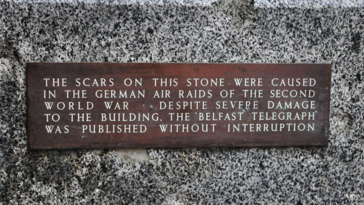 A small plaque marking damage caused to the stonework during the Belfast Blitz of 1941 on the wall of the former Registered Offices of the Belfast Telegraph newspaper on the corner of Library Street and Royal Avenue, Belfast.