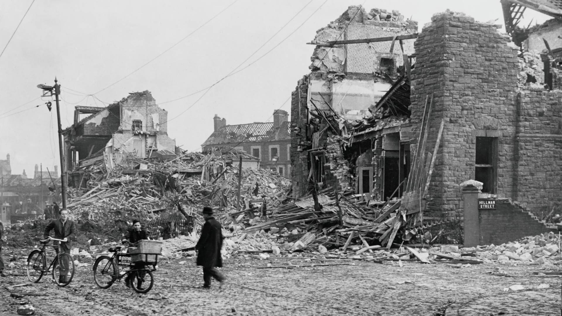 Local residents go about their day among the bomb damage at the junction of Hillman Street with Antrim Road, Belfast.