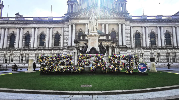 A floral sculpture by Belfast One in front of Belfast City Hall on Donegall Square North, flanked by stone columns commemorating Able Seaman James Magennis V.C. and the arrival of United States Forces in Ulster.