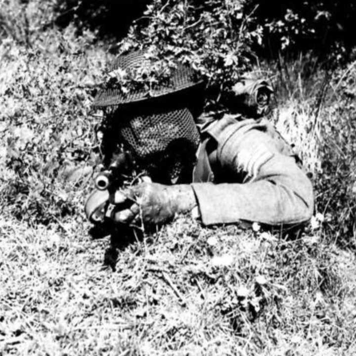 A British Army soldier with a Tommy Gun wearing camouflage veiling takes aim amidst bushes during training in Northern Ireland.