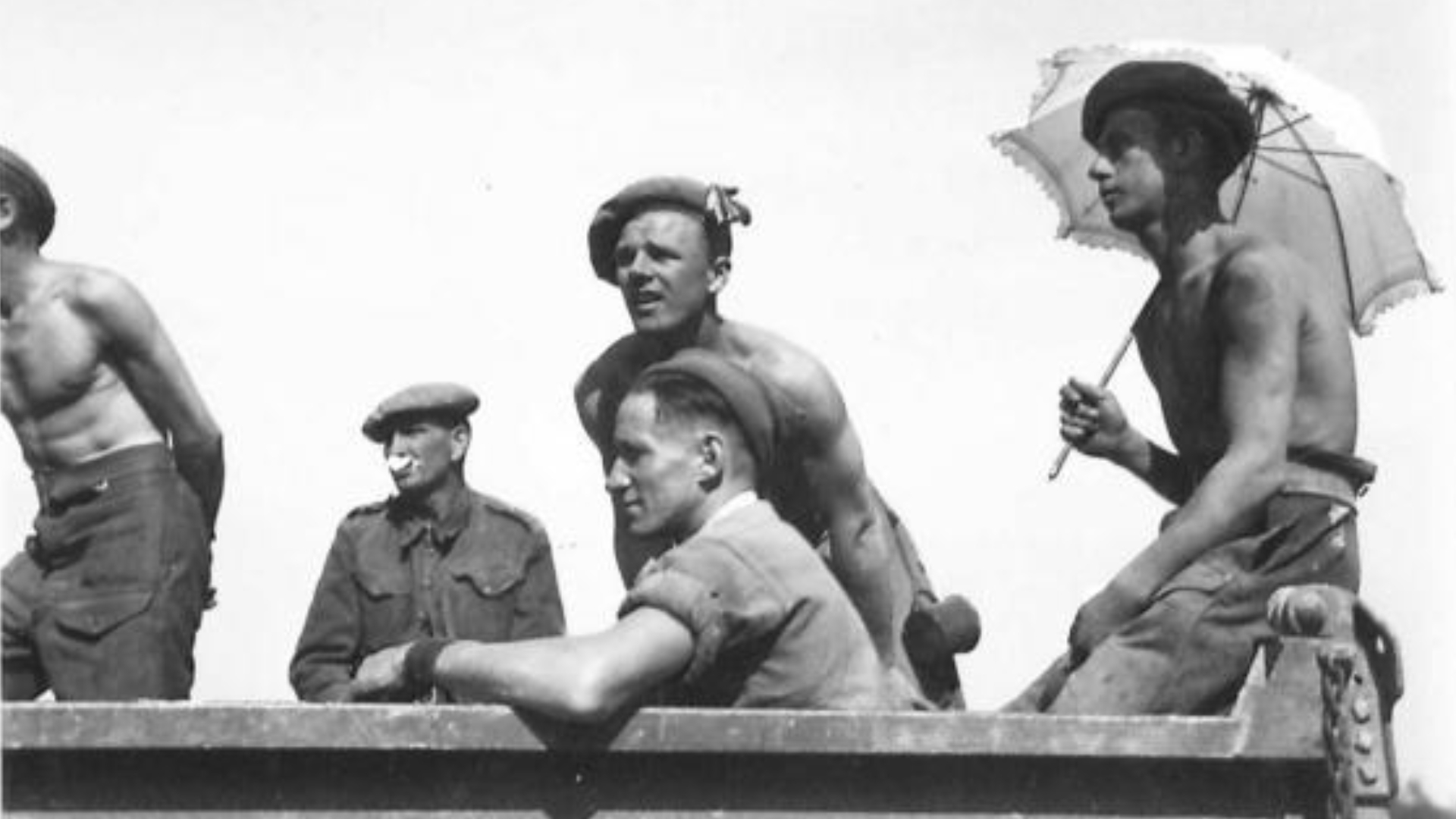 Five members of the Pioneer Corps on a lorry returning from construction work in Normandy, France. Private Charles Miles of Middlesborough, Yorkshire, England shelters from the sun beneath a parasol.