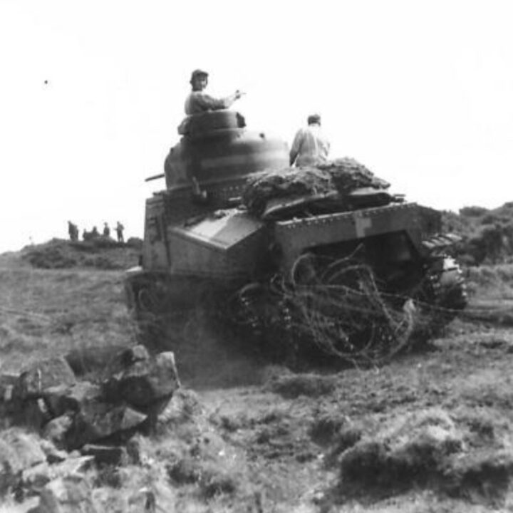 An M3 Lee Medium Tank of a United States Army Armored Division crosses rolls of barbed wire and obstacles as part of Exercise Defiance near Carrickfergus, Co. Antrim.