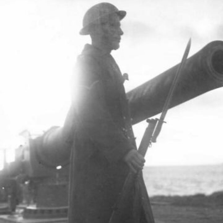 A sentry stands guard next to a 6-inch naval coastal defence gun at defences under control of 380th Battery, Royal Artillery (T.A.) at Magilligan Point, Co. Londonderry. The photo is part of a series from the visit of 'Sortie Y' to Northern Command.