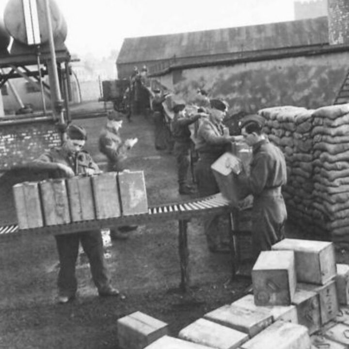 Members of the Auxiliary Territorial Service off-load empty petrol cans on to a roller conveyor where they are inspected, repaired, cleaned, and refilled at a petrol distributing centre in Northern Ireland.
